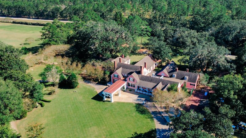Aerial view of a pink estate home among live oaks and open lawn