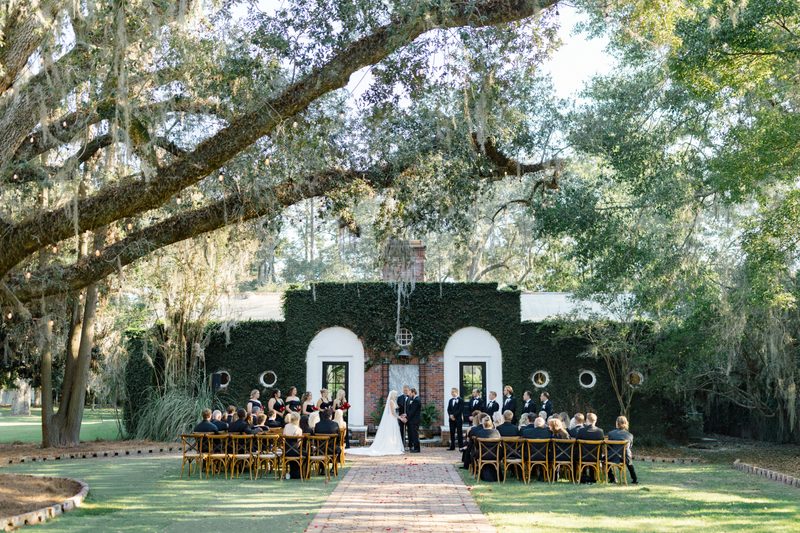Couple exchange vows before an ivy-covered wall beneath live oaks hung with Spanish moss