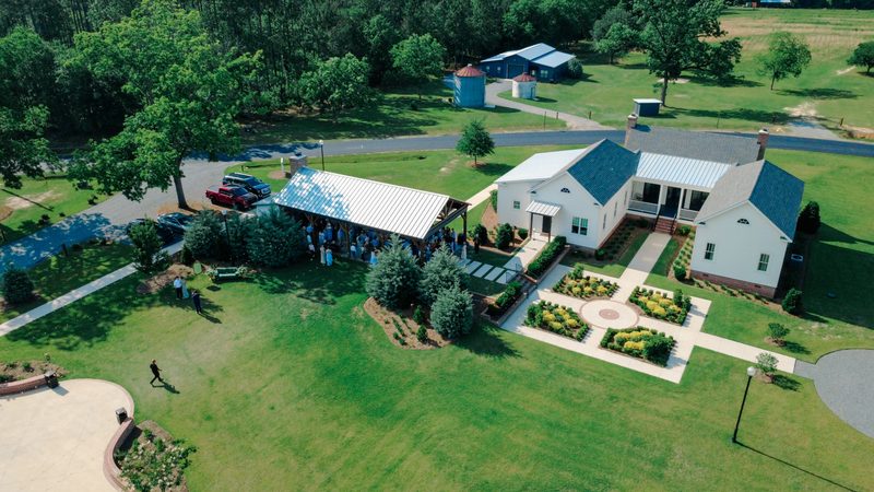 Aerial view of a white chapel and barn venue ringed by pines and green fields
