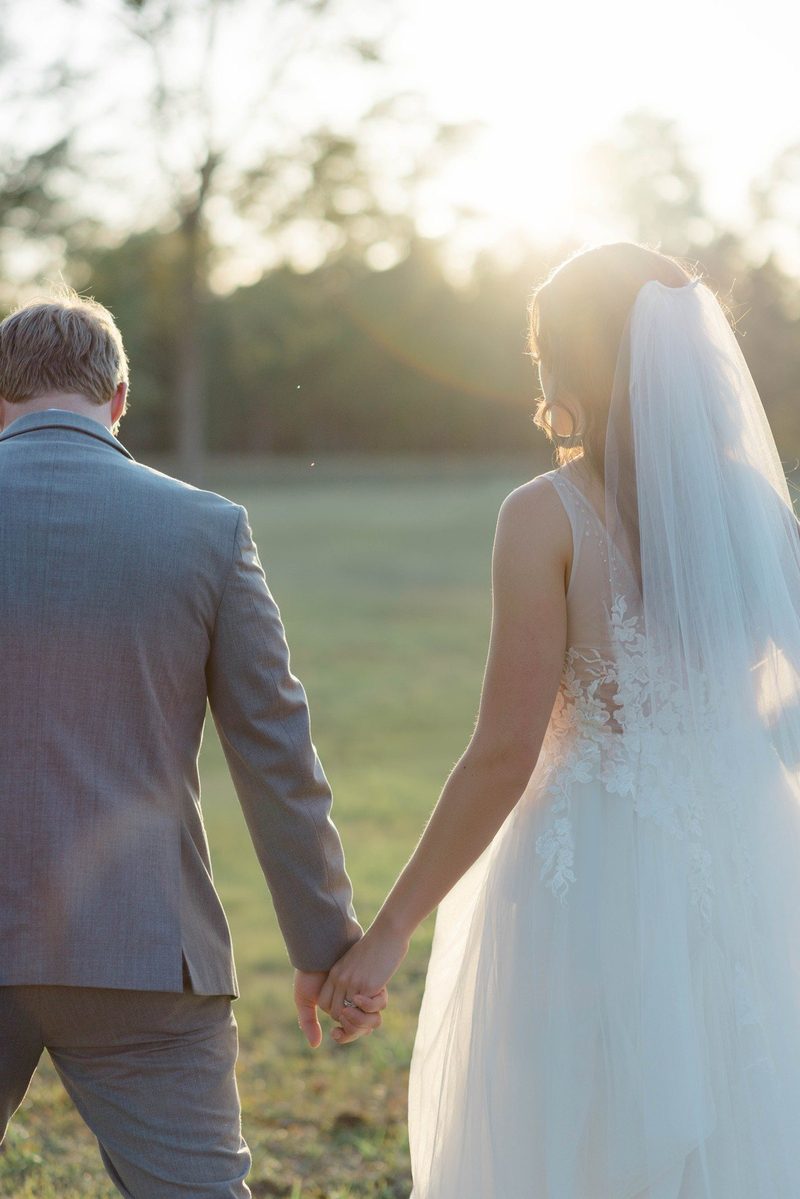 Groom and bride walk hand in hand toward the setting sun