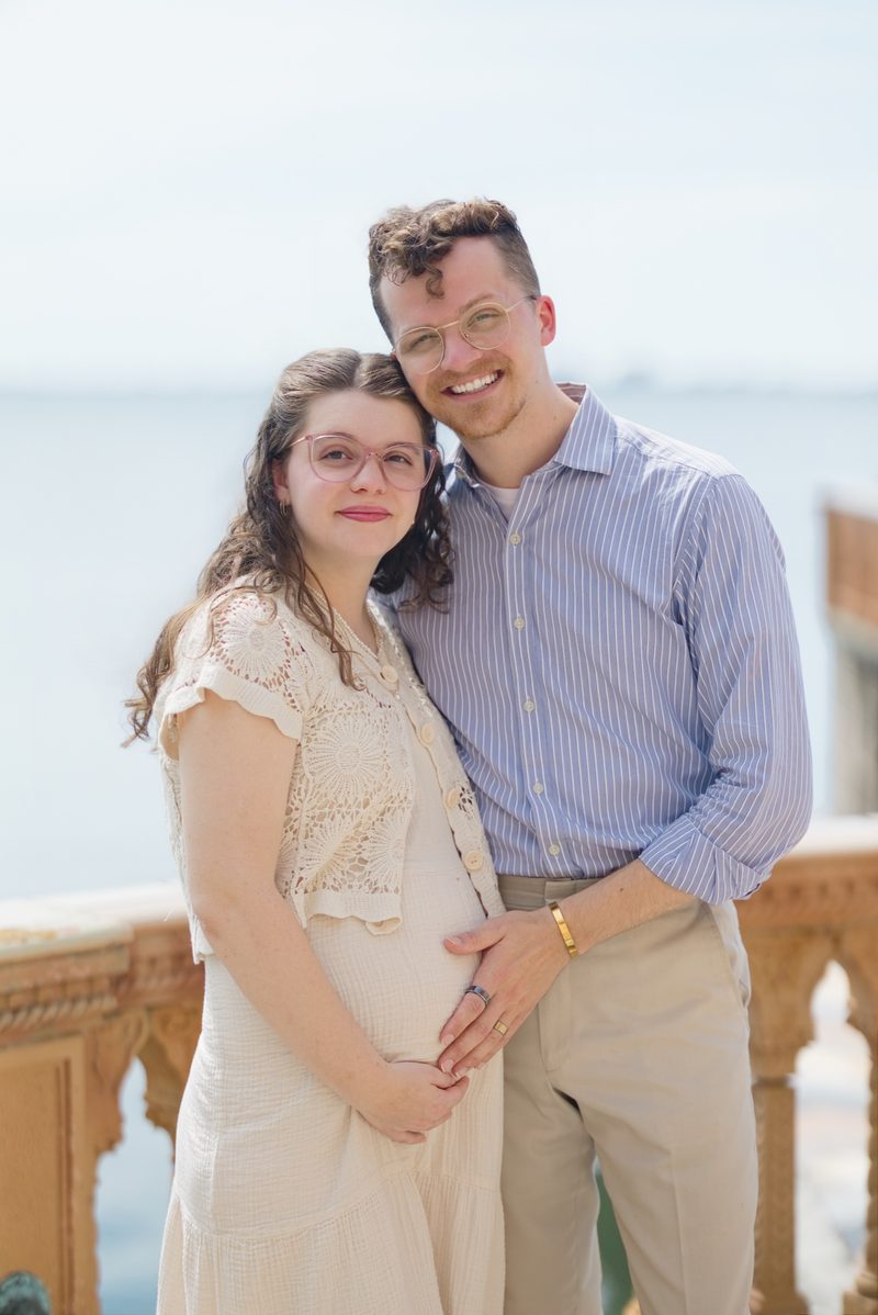 Grant and Morgan lean their heads together, smiling, with the bay behind them
