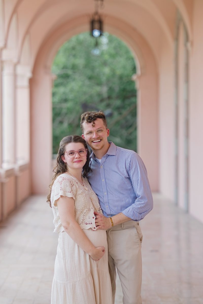 Grant and Morgan smile together under a pink arched arcade