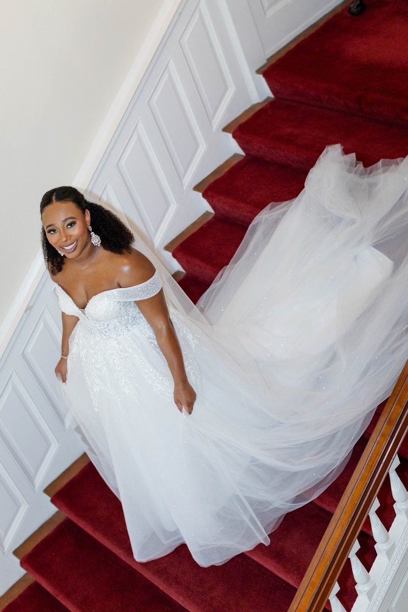 Bride in a white gown descends a red-carpeted staircase