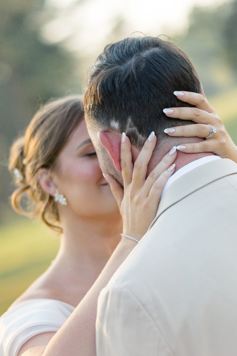 Bride's hands cradle the groom's face as they kiss in golden light