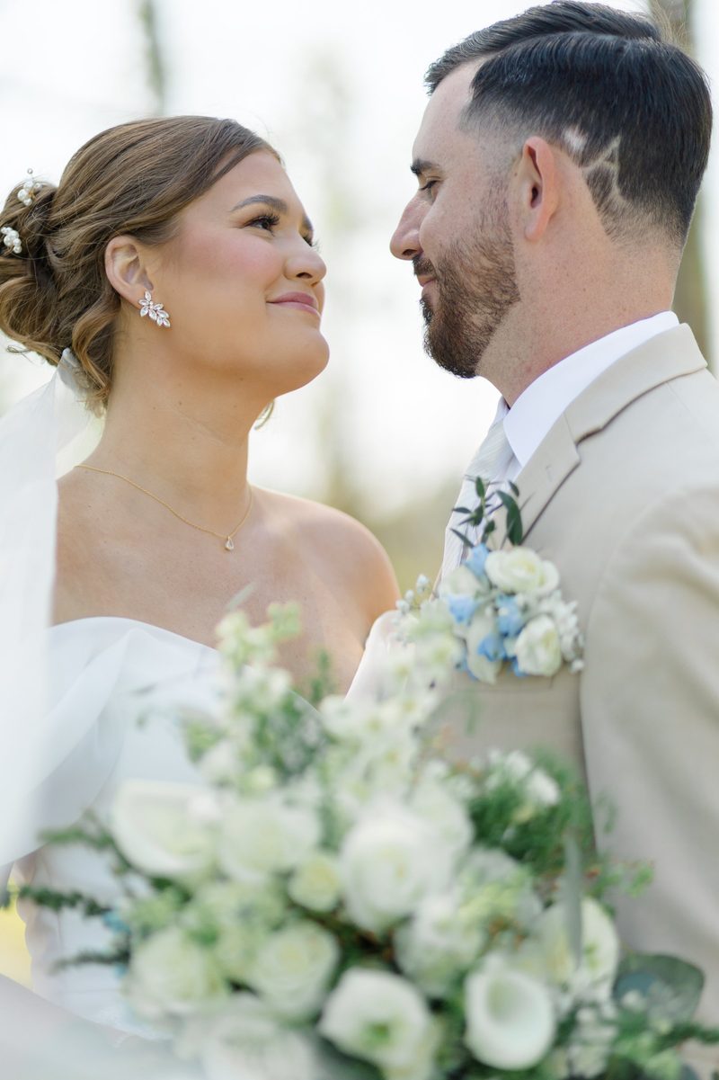 Bride and groom look at each other, her bouquet of white roses between them