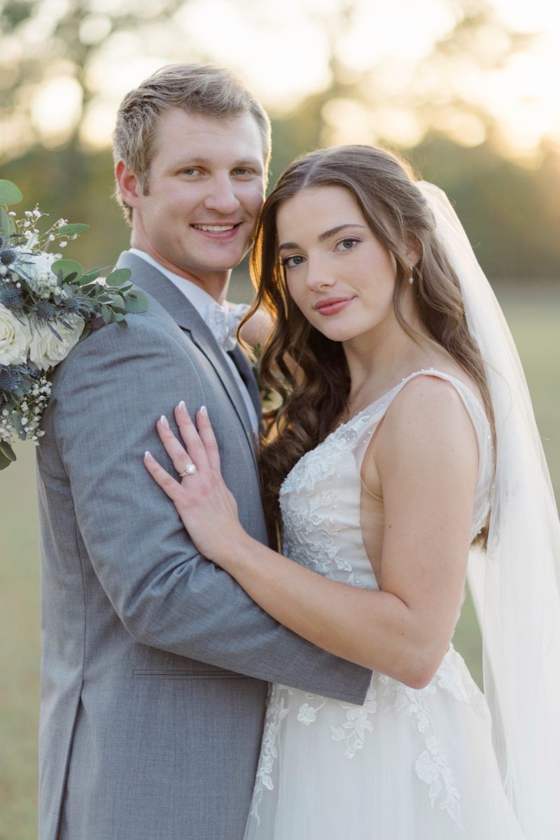 Groom and bride embrace in golden evening light, both looking into the camera