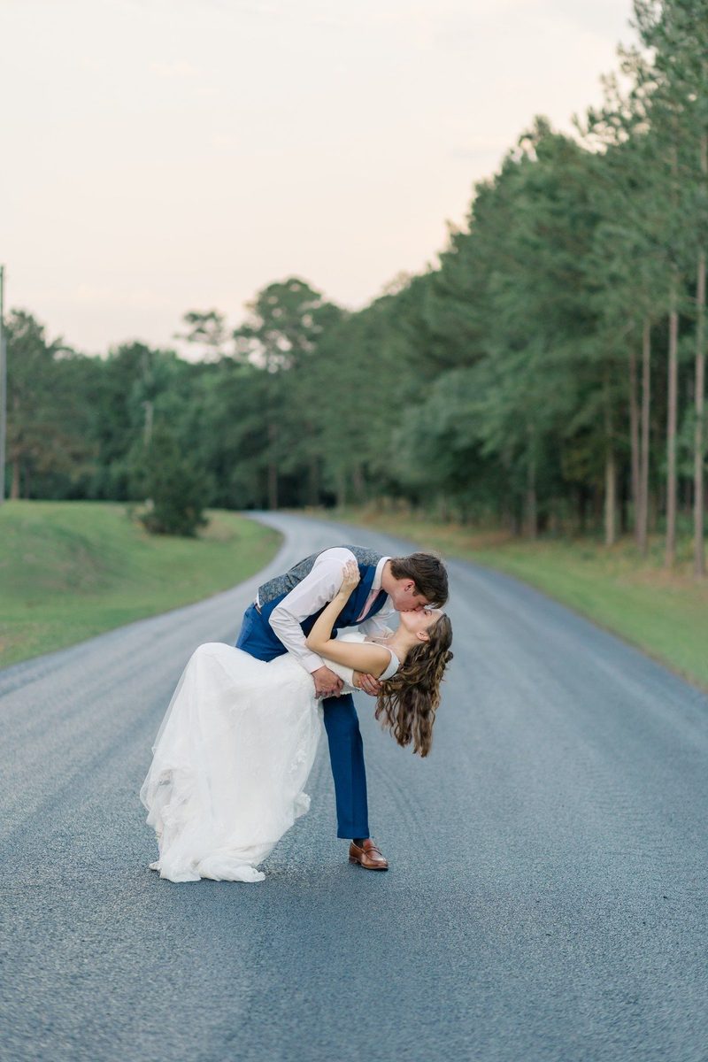 Groom dips the bride for a kiss on a tree-lined road