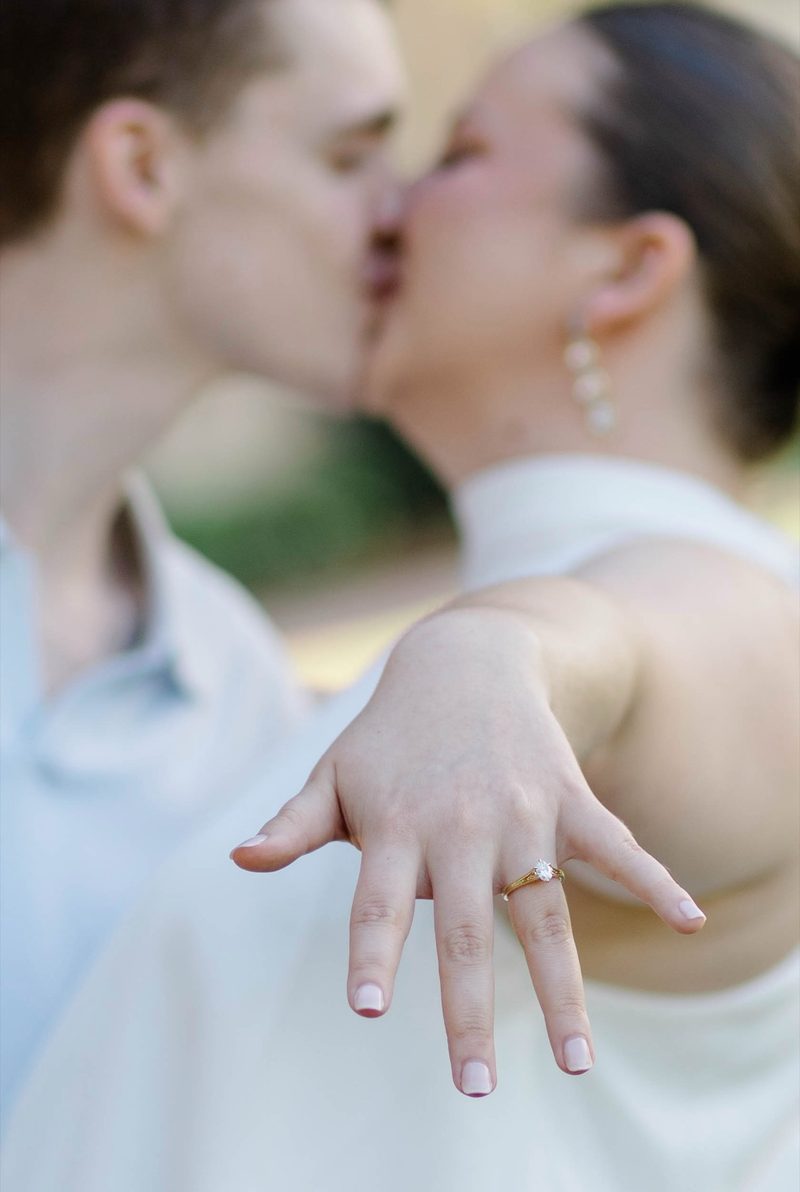 Couple kiss as she holds her engagement ring toward the camera