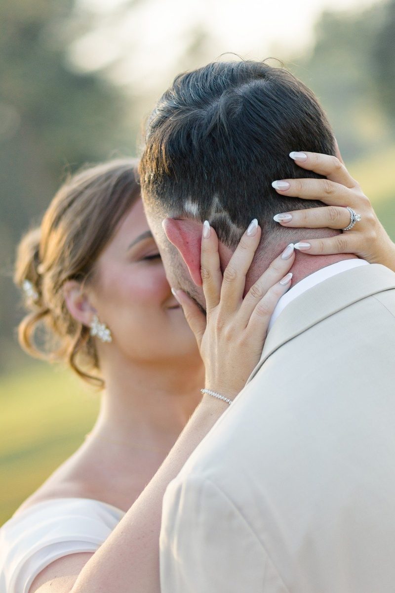 Bride cradles the groom's face in soft evening light