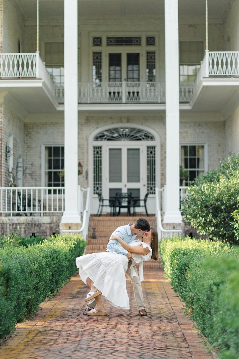 Groom dips the bride on a brick path in front of a columned home