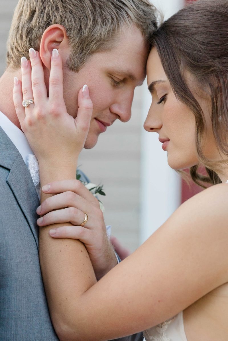 Groom and bride touch foreheads, her hand on his cheek, ring visible