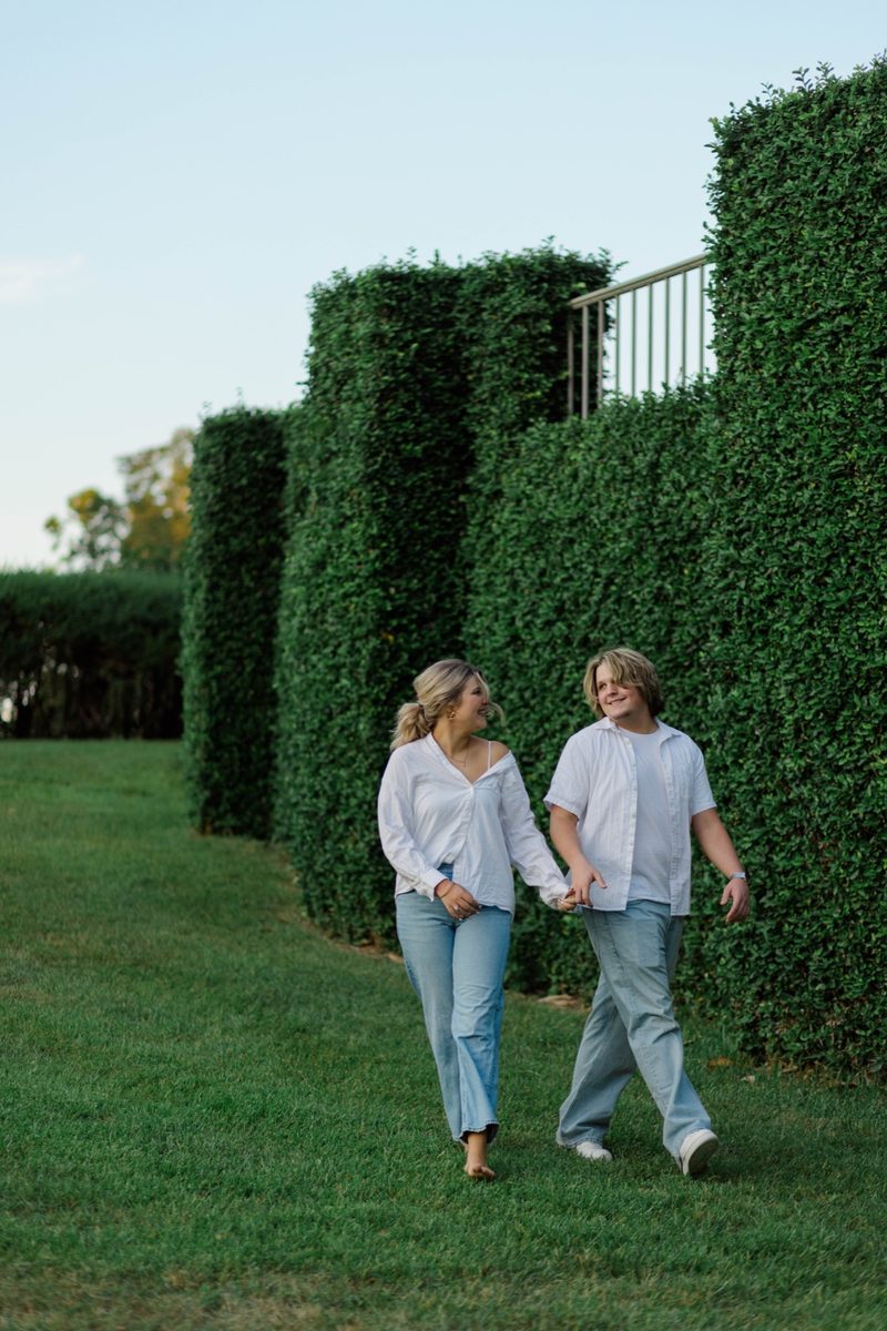 Couple walk hand in hand along a tall green hedge