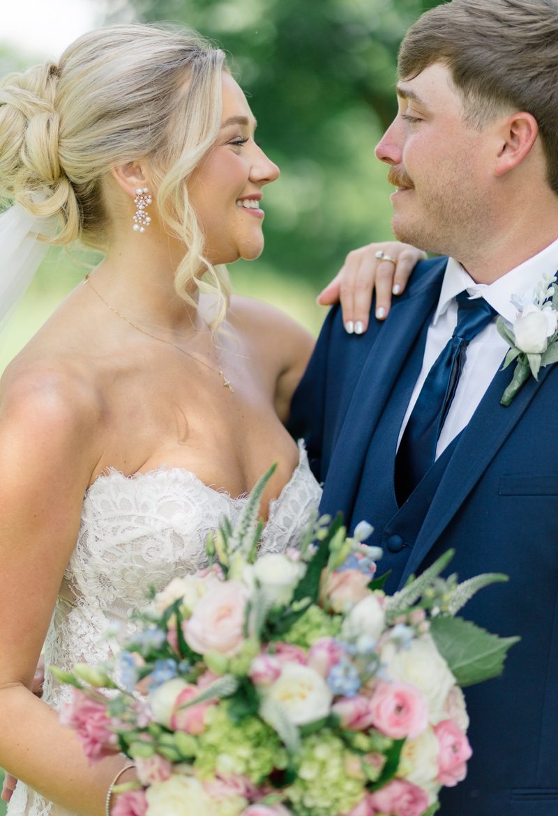 Bride and groom look at each other, her bouquet of pink and green blooms between them