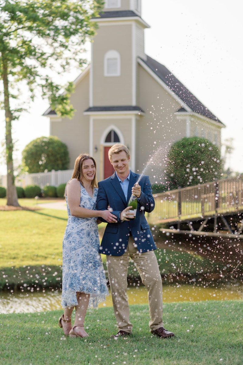 Fiancé pops champagne in front of a small chapel, the spray catching the light