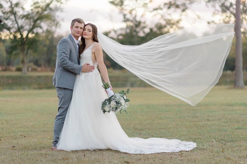Bride's veil streams out behind the couple on a lakeside lawn