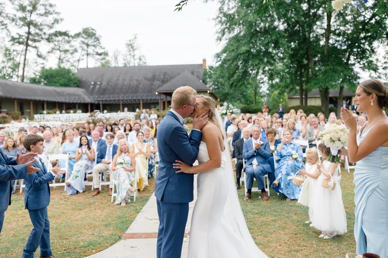 Couple kiss at the end of the ceremony as guests cheer from white chairs