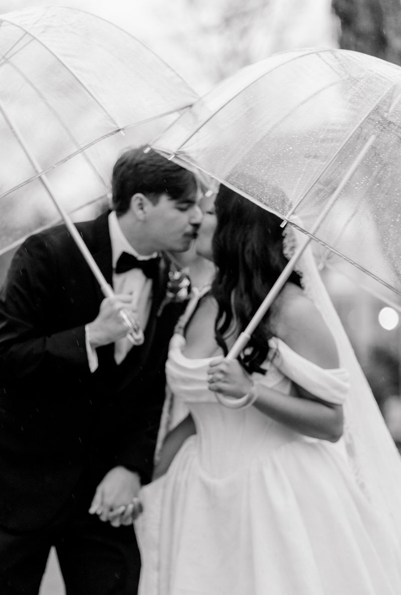Black-and-white: couple kiss beneath clear umbrellas