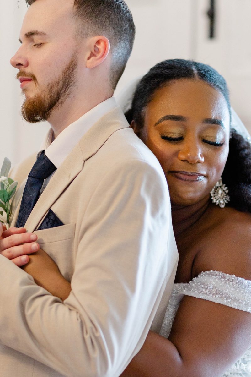 Groom and bride embrace, her eyes closed against his shoulder