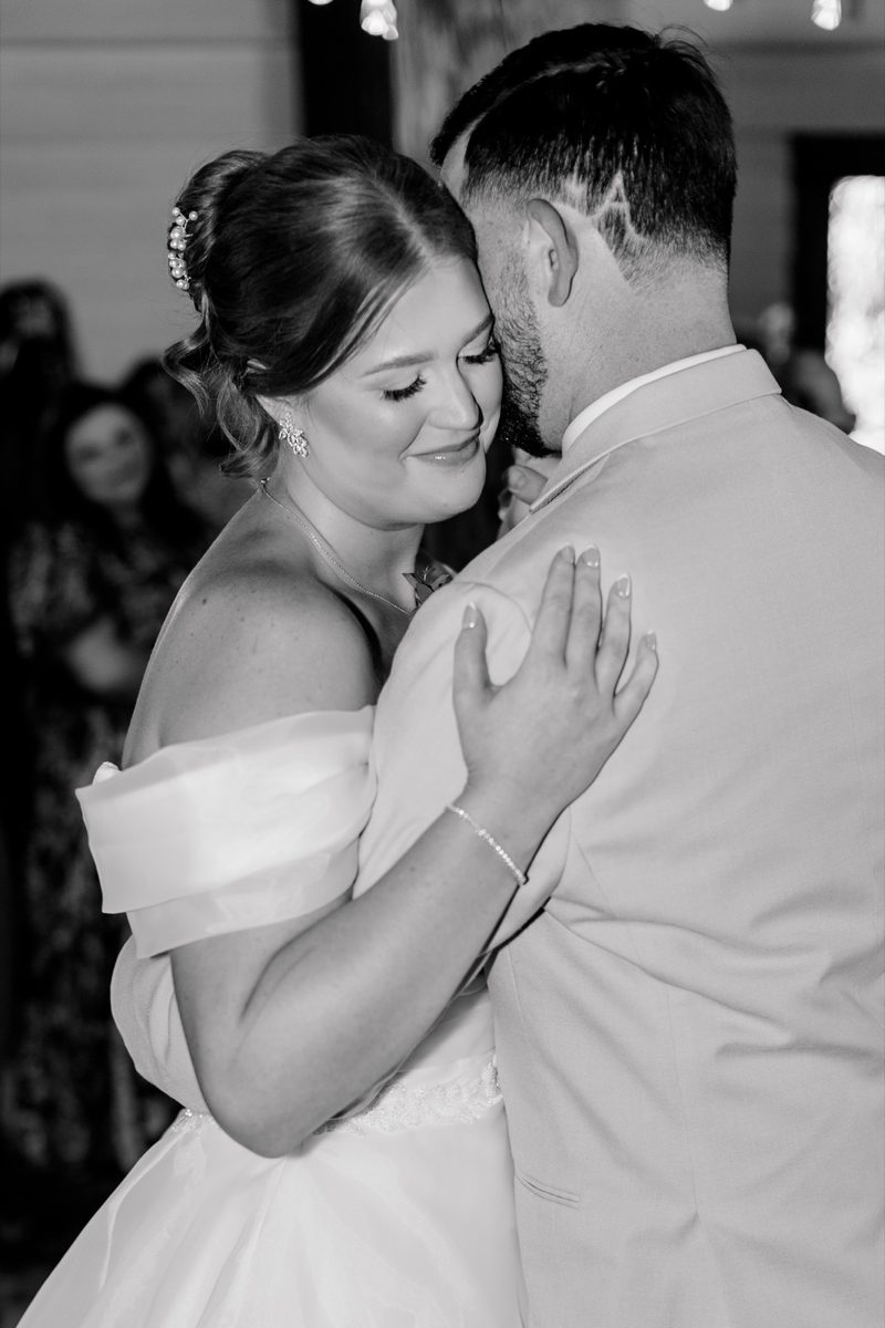 Black-and-white: couple share a slow dance, her head against his chest