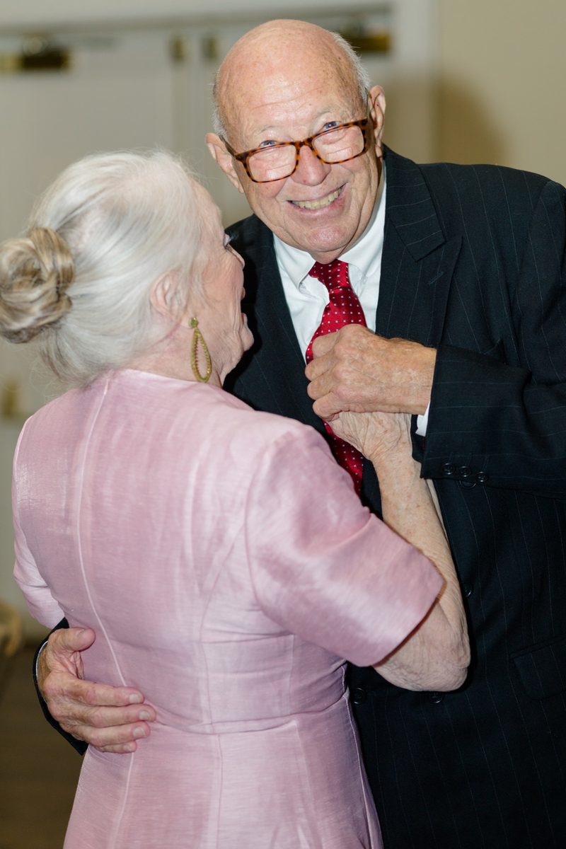 Elderly couple dance cheek to cheek, both smiling