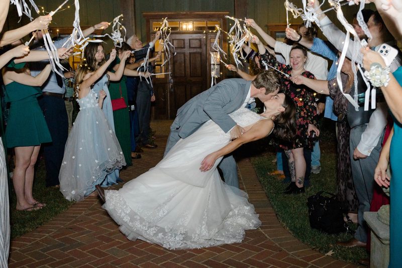Couple kiss mid-dip as guests wave ribbon wands in the send-off tunnel