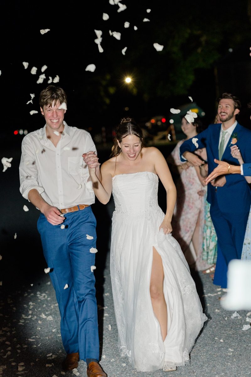 Bride and groom laugh as they walk out through a shower of petals at night